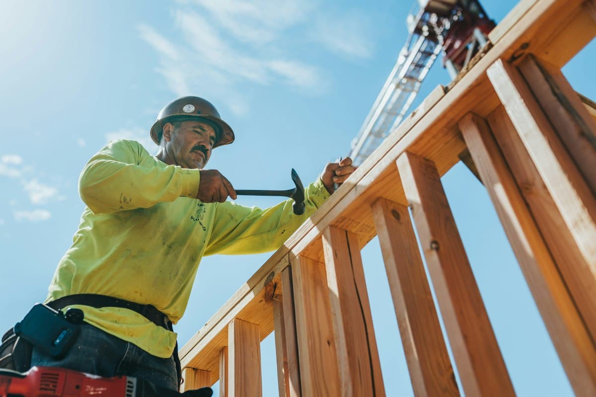 A builder in a hard hat and safety harness working on a timber structure